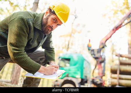 Forest lavoratore con lista di controllo durante il caricamento di registri a lungo dopo la raccolta Foto Stock