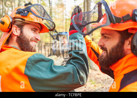Due dei lavoratori forestali come team lumberjack si donano un alto cinque al raccolto di legno Foto Stock