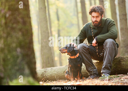 Forester è seduta su un log con un cane come un cane da caccia nei boschi Foto Stock
