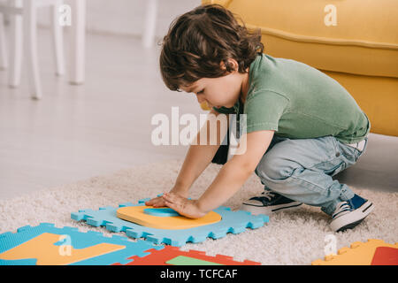 Carino il bambino in verde t-shirt giocando con tappetino puzzle Foto Stock