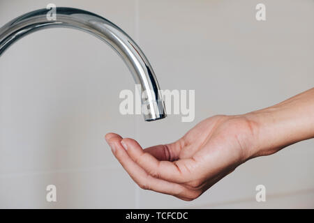 Primo piano di un uomo caucasico in interni con la mano sotto un rubinetto, in attesa per l'acqua di fuoriuscire Foto Stock