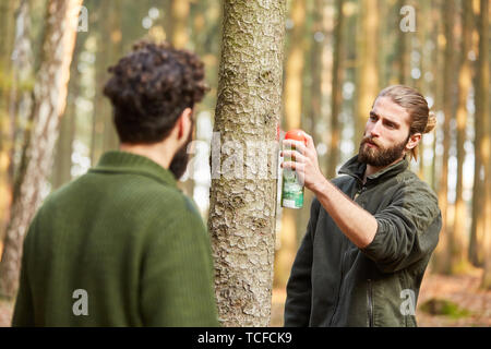 Giovani forester segna un albero con vernice rossa dalla bomboletta spray per il raccolto di legno Foto Stock