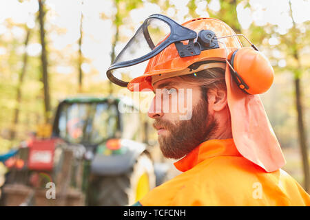 Forest agricoltore come un taglialegna in indumenti protettivi durante la raccolta di legno nella foresta Foto Stock