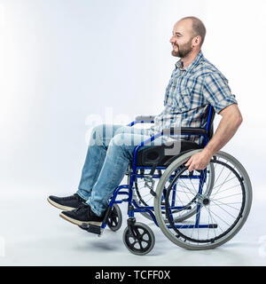 Disabili sorridente uomo seduto in una sedia a rotelle. Espressione positiva e un abbigliamento informale. Foto Stock