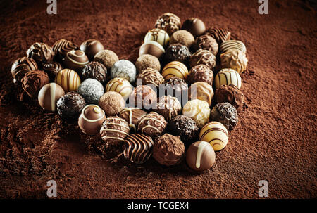 Più in bianco e nero di cioccolato confettini dolciario in forma di cuore seduti sul tappetino di polvere di cacao Foto Stock