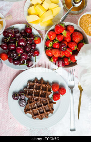 Tavolo per la prima colazione con cioccolato Banana Waffle. Il miele, burro di arachidi, fragole, Mango e le ciliegie nelle vicinanze Foto Stock