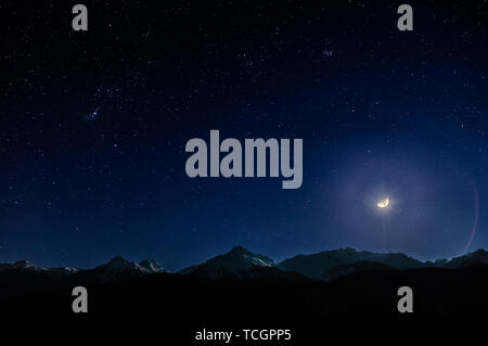 Coperta di neve la gamma della montagna di notte sotto un cielo stellato e una luminosa luna. Foto Stock