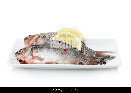 Pesce fresco con limone e pepe sulla piastra isolata su bianco