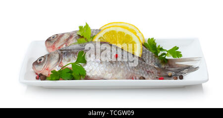Pesce fresco con limone e prezzemolo sulla piastra isolata su bianco