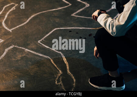 Vista parziale di investigatore seduto vicino a Chalk outline a scena del crimine Foto Stock