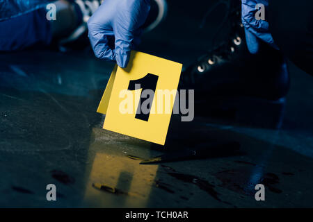 Vista parziale di investigatore nei guanti di gomma con una prova di marcatore alla scena del crimine Foto Stock