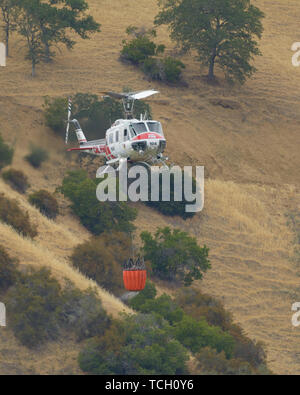 Una licenza CAL Fire elicottero volando attraverso le colline con un secchio di acqua. Lago Berryessa, CALIFORNIA, STATI UNITI D'AMERICA Foto Stock