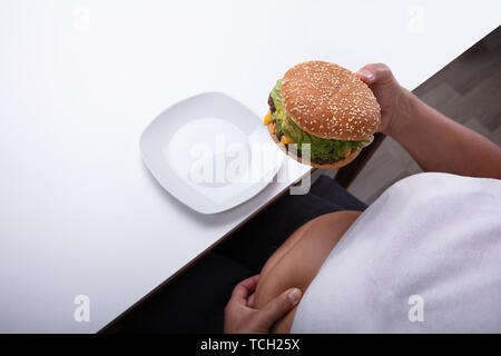 Una vista in pianta di una Donna sovrappeso holding Hamburger in mano Foto Stock