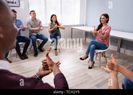 Un gruppo di giovani sordi di apprendimento gesto segno da donna seduta su una sedia Foto Stock