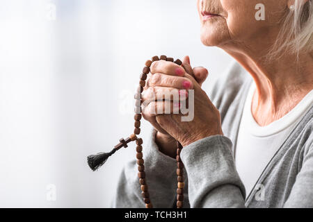 Vista parziale di senior donna orante con il rosario in legno Foto Stock