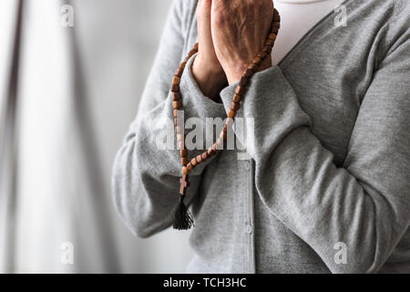 Vista parziale di senior donna orante con il rosario in legno Foto Stock