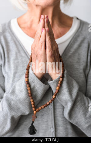 Vista parziale di senior donna orante con il rosario in legno Foto Stock