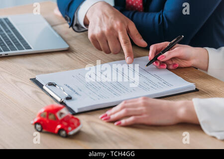 Vista ritagliata della trattativa auto puntando al posto della firma di un accordo di prestito nei pressi di donna tenendo pen Foto Stock