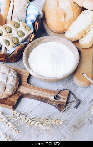 Diversi tipi di Italiano tradizionale di pane appena sfornato, vari tipi di pane e panini con ciotola di farina a fontana sul tavolo di legno dello sfondo. Rustico stile vintage. Foto Stock