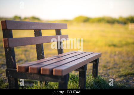 Un banco di solitario in un campo nel mezzo del Regno Unito prese durante un tramonto basso Foto Stock