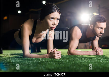 Messa a fuoco selettiva della donna facendo esercizio tavoloni vicino all uomo bello sull'erba Foto Stock