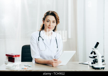 Sorridente medico in camice bianco con utilizzando uno stetoscopio digitale compressa in clinica Foto Stock