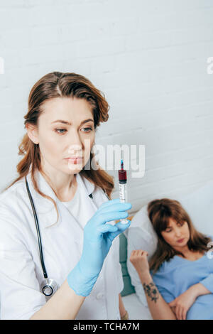 Donatore sdraiato sul letto e medico tenendo la siringa con il campione di sangue Foto Stock