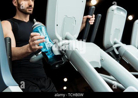 Messa a fuoco selettiva di bello uomo barbuto tenendo la bottiglia sport lavoro su cyclette Foto Stock