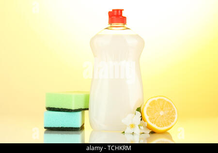 Detersivo liquido per stoviglie con spugne e limone con fiori su sfondo giallo Foto Stock