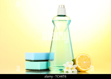 Detersivo liquido per stoviglie con spugne e limone con fiori su sfondo giallo Foto Stock