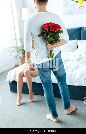 Vista posteriore di uomo con rose rosse dietro torna in camera da letto Foto Stock