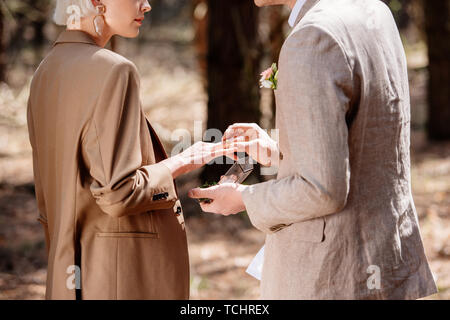 Vista parziale dell'uomo a mettere su l'anello nuziale sulla donna dito nella foresta Foto Stock