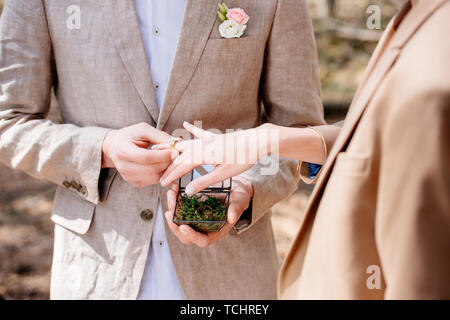 Vista ritagliata dello sposo e della sposa di mettere l'anello nuziale sul dito Foto Stock