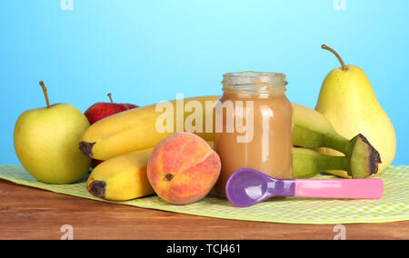 Vaso con frutta Alimenti per neonati, cucchiaio e frutti sul tovagliolo colorato su sfondo blu Foto Stock