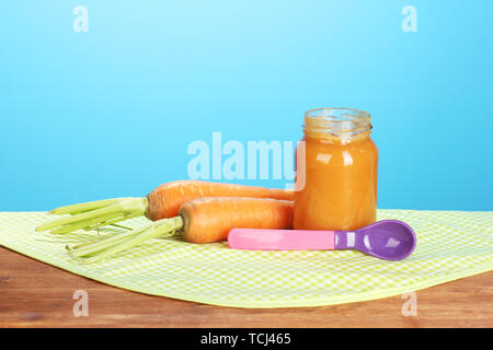 Vaso con omogeneizzati alla carota, cucchiaio e carote sul tovagliolo colorato su sfondo blu Foto Stock