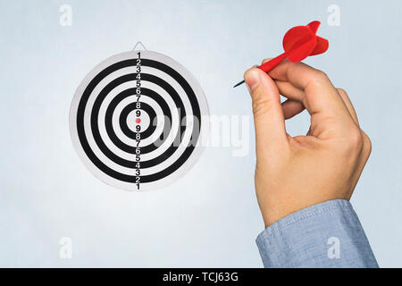 Una mano che tiene un dardo ottenere pronto a mirare il dartboard sulla parete blu. una mano d'uomo getta un dart a bersaglio. round target Foto Stock