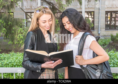 Due belle gli studenti di diverse nazionalità sono in piedi presso il recinto dell'Università insieme la lettura di un libro Foto Stock