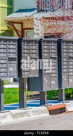 Telaio Panorama fila di cassette postali di cluster con scomparti numerati su un marciapiede soleggiato Foto Stock