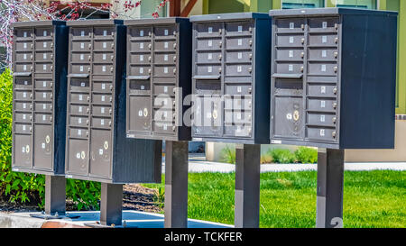 Panorama fila di cassette postali di cluster con scomparti numerati su un marciapiede soleggiato Foto Stock