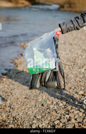 Garbage in natura, la pulizia dell'ambiente in primavera sul fiume dalle macerie di una donna in lattice monouso guanti blu nel grande blu Foto Stock