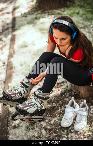 Donna allacciamento rulli mentre seduto nel parco e ascolto di musica con cuffie Foto Stock