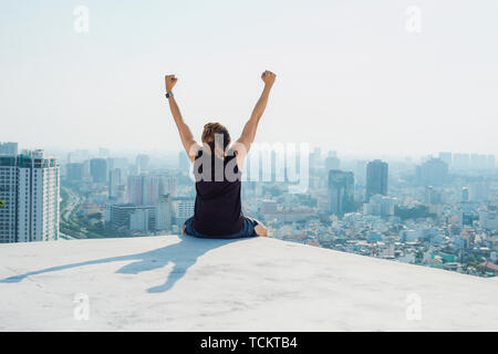 Uomo seduto sul tetto nero e mostra fino a mano con cielo blu di sfondo e sunshine,combattimenti uomo sul tetto Foto Stock