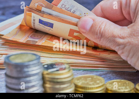 Macro di mano femminile prendendo le banconote da un mucchio di denaro Euro, davanti sono giacenti sfocata pile di monete Foto Stock