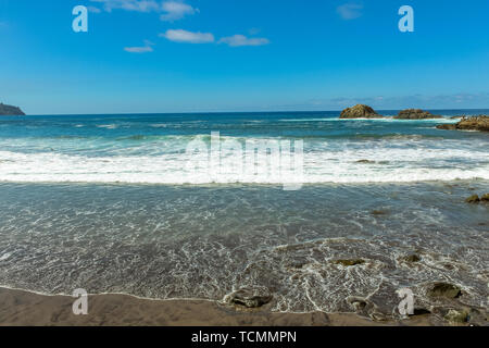 Vista panoramica di Aimasiga spiaggia con sabbia nera vulcanica e lone rocce che sporgono dalla schiuma del mare sulla costa settentrionale dell'isola Tenerife, Spagna Foto Stock