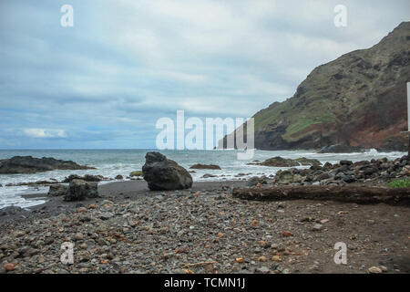 Alta ripida roccia lavica a strapiombo sul a est di Tenerife. Rocce solitarie fuori dell'acqua. Spiaggia di sabbia nera. Mare azzurro orizzonte, cielo naturale indietro Foto Stock