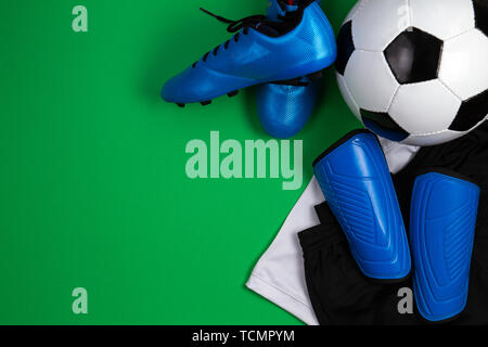 Pallone da calcio, scarpe blu, bitte, bianca t-shirt e pantaloncini neri su sfondo verde. Piatto, laici vista superiore Foto Stock