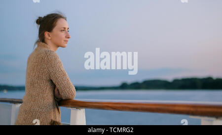 Donna ammirando il paesaggio dal ponte della nave da crociera dopo il tramonto Foto Stock