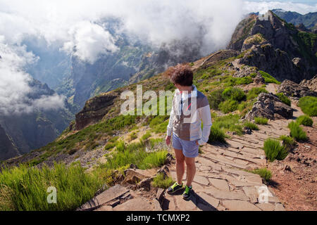 Giovane donna in piedi sul bordo del burrone e guardando verso il basso. Pico do Arieiro picco di montagna su isola portoghese di Madeira Foto Stock