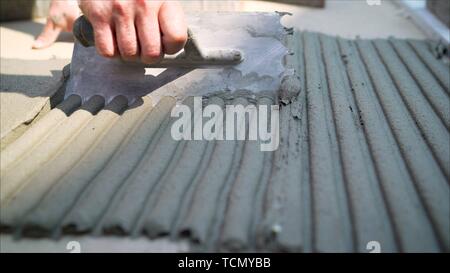 Lavoratore con una spatola e mortaio. Il builder sulle sue ginocchia appiattisce la malta di cemento con una spatola manuale per la fabbricazione di lastre per pavimentazione. Foto Stock