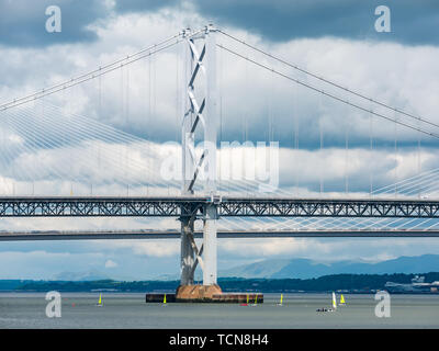 South Queensferry, Scotland, Regno Unito, 9 giugno 2019 UK Meteo: luce drammatica e nuvole scure raccogliere sul Forth Road Bridge e la Queensferry incrocio con colore giallo brillante derive creando un stark il colore e le dimensioni di contrasto nel fiume Forth Foto Stock